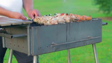 Man is Cooking Pork Barbecue in Summer in the Daytime Outdoors - Static Shot, Slow Motion. Turning Barbecue on Skewers. Hot Grilled Kebab on the Coals. Roasted or Grilled BBQ on a Skewer or Spit
