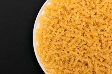 Pişmemiş Fusilli Makarna Siyah Arkaplanda Beyaz Tabakta Yatıyor. Çiğ ve kuru makarna. Sağlıksız ve Yağlı Gıda - Üst Görünüm