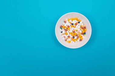 Küresel İlaç Endüstrisi ve İlaç Ürünleri - Mavi Arkaplan Üzerine Beyaz Tabakta Renkli Haplar ve Kapsüller