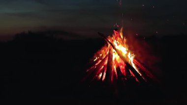 Big Burning Campfire at Summer Night against the Blue Sky. Wood on Fire. Flying Sparks. Travel and Tourism Concept. Giant Flaming Bonfire - Static Shot, Slow Motion