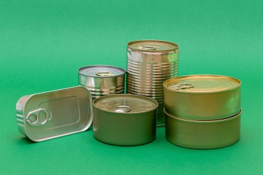 Yeşil Arkaplanda Boş Kenarlı İstiflenmiş Teneke Kutular Grubu. Konserve yiyecekler. Güvenli ve uzun vadeli yiyecek depolamak için farklı alüminyum kutular. Çelik Mühürlü Yiyecek Depolama Kutuları