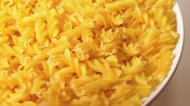 Beyaz Plaka 'da pişmemiş Fusilli Makarna Beyaz Arkaplan' a karşı dönüyor. Şişman ve Sağlıksız Yemek. Kuru Spiral makarna. İtalyan Kültür ve Mutfağı. Çiğ Altın Makarna