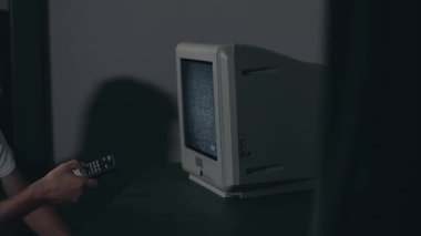 Kırık Televizyon veya TV Propagandası. Zihin Kontrolü - Beyaz tişörtlü Zombi Karanlık Oda 'daki Eski TV kanallarını değiştirdi. TV Sinyal Arama. Ekrandaki bozulma. Ortalama Yakın Çekim, Film Tanesi
