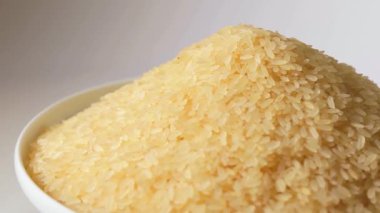 Kuru, haşlanmamış pirinç yığını, Beyaz Arkaplan 'a karşı dönüyor. Çiğ Uzun Taneli Pirinç Yığını. Asya mutfağı ve kültürü. Sağlıklı beslenme malzemeleri. Diyet Yemekler