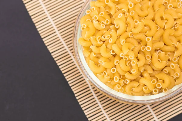 未烹调的Chifferi Rigati Pasta Glass Jar Bamboo Mat Black Background 脂肪和不健康的食物 — 图库照片