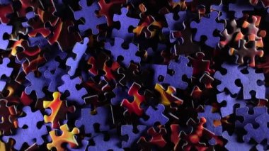 Background of Colored Puzzle Pieces that Slowly Rotating Counterclockwise - Top View. Texture of Incomplete Red and Blue Jigsaw Puzzle with Low Key Light - Left Rotation