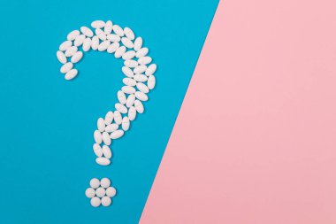 Beyaz haplar ve tabletlerden yapılmış soru işareti mavi ve pembe arka planda yatıyor. Global İlaç Endüstrisi ve Tıbbi Ürünler