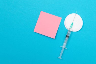 Aşı, Bağışıklık Bilimi veya Yeniden Aşılama Konsepti - Bir Hastane veya Klinikte Mavi Masa üzerinde yatan Tıbbi Tek Kullanılabilir Şırınga. Boş Pembe Yapışkan Not - Uzayı Kopyala ile Moklonla