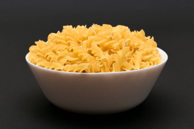 White Bowl 'daki pişmemiş Fusilli Makarna Siyah Masa' da. Çiğ ve kuru makarna. Sağlıksız ve şişman yiyecekler. İtalyan Kültürü