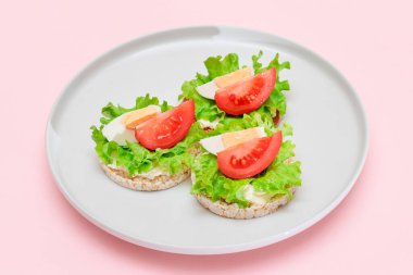 Domatesli pirinç keki sandviç, beyaz tabakta marul ve yumurta. Kolay Kahvaltı 'da. Diyet yemek. Hızlı ve sağlıklı sandviçler. Lezzetli dolgulu kızarmış ekmek. Sağlıklı Beslenme Atıştırması