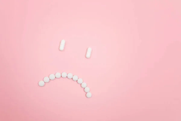 製薬会社の責任だ 白い丸薬で作られた悲しい笑顔の顔 ピンクの背景に横たわっています 世界の医薬品産業と医薬品 — ストック写真