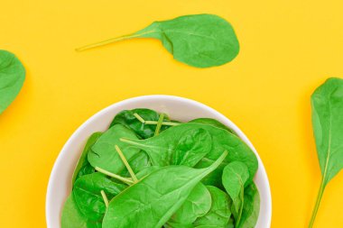 Taze Ispanak Yaprakları Beyaz Kasede Sarı Arkaplanda - Üst Manzara. Vejetaryen ve Vejetaryen Kültürü. Çiğ yemek, yeşil yapraklar. Sağlıklı Beslenme