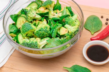 Taze Yeşil Avokado Salatası, Brokoli, Ispanak ve Salatalık ve Soya Sosu ve Tahta Kesme Kurulunda Kırmızı Acı Biber. Vejetaryen salatası. Vejetaryen Kültürü. Çiğ yemek. Sağlıklı beslenme ve sebze diyeti