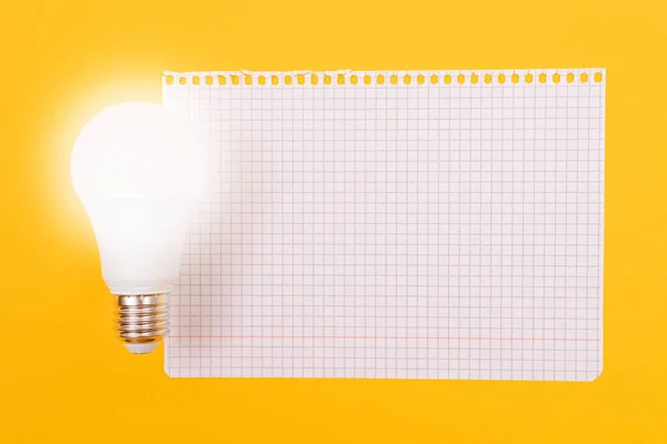 A Power Saving Lamp with Notepad Lying on Yellow Table, Blank Template with Copy Space - Top View, Flat Lay