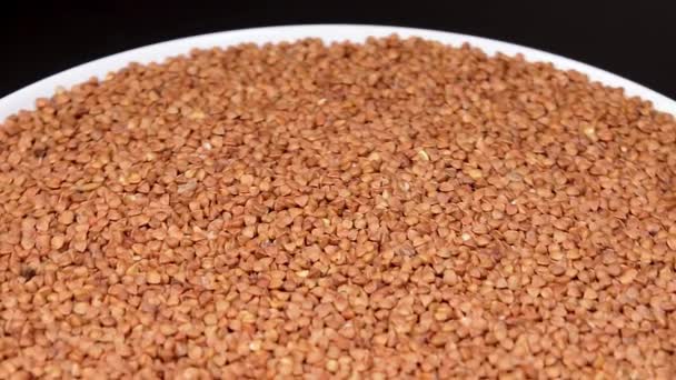Dry Uncooked Brown Buckwheat Groats White Plate Rotating Black Background — Αρχείο Βίντεο