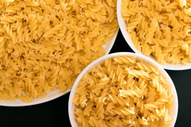 Pişmemiş Fusilli Makarna Siyah Arkaplanda Beyaz Tabakta Yatıyor. Çiğ ve kuru makarna. Sağlıksız ve Yağlı Gıda - Üst Görünüm