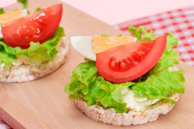 Domatesli Rice Cake Sandviç, Tahta Kesme Kurulunda Marul ve Yumurta. Kolay Kahvaltı 'da. Diyet yemek. Hızlı ve sağlıklı sandviçler. Lezzetli dolgulu kızarmış ekmek. Sağlıklı Beslenme Atıştırması