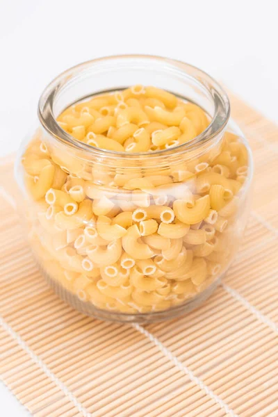 未烹调的Chifferi Rigati Pasta Glass Jar Bamboo Mat White Background 脂肪和不健康的食物 — 图库照片