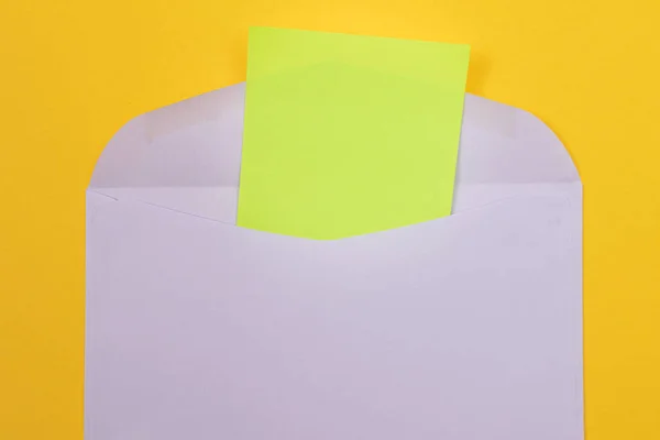 紙の中の空白の緑のシートを持つバイオレットエンベロープ 黄色の背景に横たわっています コピースペースでモックアップ 郵便または通知の受信 郵便はがきの送信 トップビュー フラットレイ — ストック写真