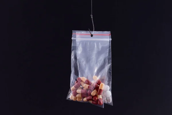 医薬品トラップと薬物中毒 黒の背景に釣りフック上の小さなジップロックバッグにぶら下がっている色の丸薬や錠剤 — ストック写真