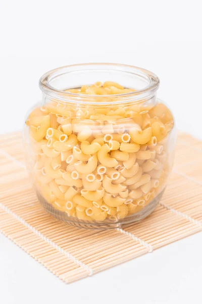 未烹调的Chifferi Rigati Pasta Glass Jar Bamboo Mat White Background 脂肪和不健康的食物 — 图库照片