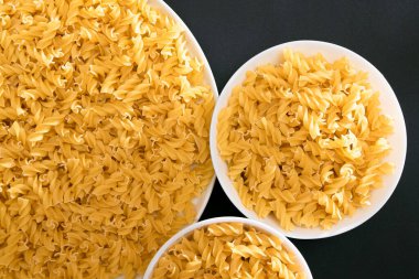 Pişmemiş Fusilli Makarna Siyah Arkaplanda Beyaz Tabakta Yatıyor. Çiğ ve kuru makarna. Sağlıksız ve Yağlı Gıda - Üst Görünüm