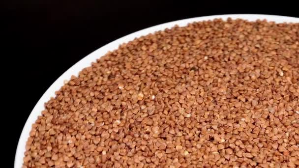 Dry Uncooked Brown Buckwheat Groats White Plate Rotating Black Background — Videoclip de stoc