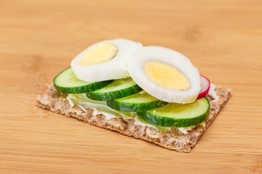 Bambu kesme tahtasında taze salatalık, yumurta, krem peynir ve turplu tam tahıllı gevrek. Kolay Kahvaltı 'da. Hızlı ve sağlıklı sandviçler. Lezzetli dolgulu kızarmış ekmek. Sağlıklı Beslenme Atıştırması