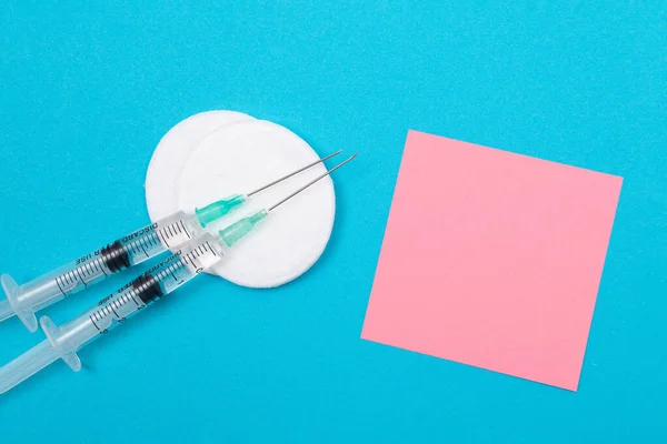 stock image Vaccination, Immunology or Revaccination Concept - Two Medical Disposable Syringe Lying on Blue Table in Doctors Office in a Hospital or Clinic. Blank Pink Sticky Note - Mock Up with Copy Space