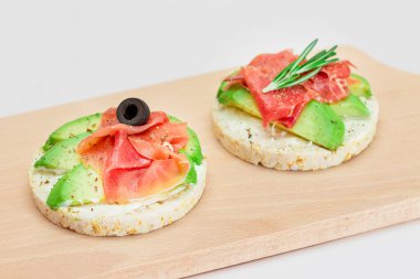 Tahta Kesme Kurulu 'nda Avocado, Jamon, Zeytin ve Rosemary ile Rice Cake Sandviçi. Kolay Kahvaltı 'da. Hızlı ve sağlıklı sandviçler. Lezzetli dolgulu kızarmış ekmek. Sağlıklı Beslenme Atıştırması