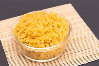Cam kavanozda pişmemiş Fusilli Makarna Bambu Mat üzerinde Kara Arkaplanda. Şişman ve Sağlıksız Yemek. Klasik kuru sarmal makarna. İtalyan Kültür ve Mutfağı. Çiğ Makarna