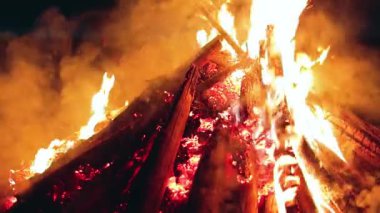 Big Campfire is Burning Down in Early Morning or Evening against the Blue Sky. Wood on Fire. Flying Sparks. Travel and Tourism Concept. Remains of a Giant Bonfire at Summer - Static Shot, Slow Motion