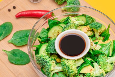 Taze Yeşil Avokado Salatası, Brokoli, Ispanak ve Salatalık ve Soya Sosu ve Tahta Kesme Kurulunda Kırmızı Acı Biber. Vejetaryen salatası. Vejetaryen Kültürü. Çiğ yemek. Sağlıklı beslenme ve sebze diyeti