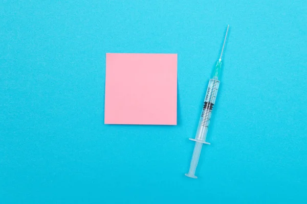 stock image Vaccination, Immunology or Revaccination Concept - A Medical Disposable Syringe Lying on Blue Table in Doctors Office in a Hospital or Clinic. Blank Pink Sticky Note - Mock Up with Copy Space