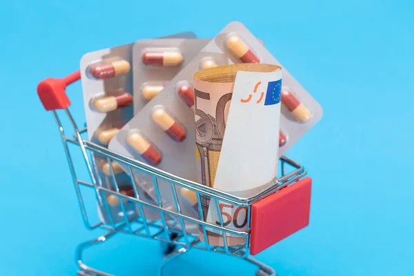 Buying Medicines. Drug Addiction Concept: Pills and Capsules in Shopping Cart on Blue Background. Global Pharmaceutical Industry and Big Pharma. Ordering Pharmaceutical Products