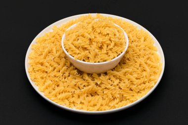 Pişmemiş Fusilli Makarna Siyah Arkaplanda Beyaz Tabakta Yatıyor. Çiğ ve kuru makarna. Sağlıksız ve şişman yiyecekler