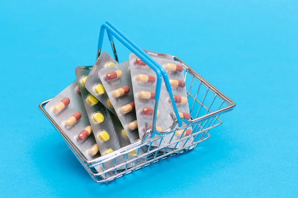 Buying Medicines. Drug Addiction Concept: Pills and Capsules in Shopping Basket on Blue Background. Global Pharmaceutical Industry and Big Pharma. Ordering Pharmaceutical Products