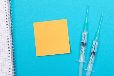 Aşılama, Bağışıklık Bilimi veya Yeniden Aşılama Konsepti - Bir Hastane veya Klinikte Mavi Masada Yatan İki Tıbbi Tek Kullanım Şırıngası. Boş Turuncu Yapışkan Not - Kopya Boşluğu ile Mock Up