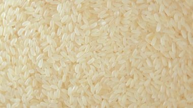 Kuru, haşlanmamış pirinç arka planı yavaşça sola doğru dönüyor. Çiğ Uzun Taneli Pirinç. Asya mutfağı ve kültürü. Sağlıklı beslenme malzemeleri. Diyet Yemekler