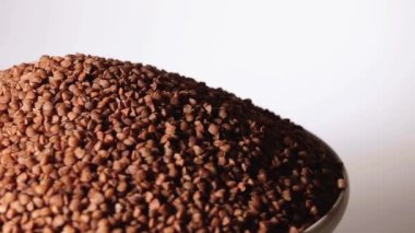 Dry Uncooked Brown Buckwheat Groats Heap on White Plate Rotating against White Background. Raw Large Buckwheat Grains. Russian, Ukrainian and Belarusian Culture
