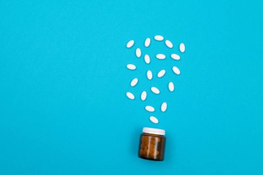 Küresel İlaç Endüstrisi ve İlaç Ürünleri - İlaç Konteynırından Dağılmış Beyaz Haplar veya Tabletler, Mavi Arkaplanda Yatanlar