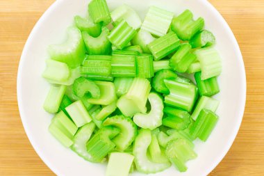 Bambu kesme tahtasında taze doğranmış kereviz dilimleri beyaz kasede. Vejetaryen ve Vejetaryen Kültürü. Çiğ yemek. Negatif Kalori İçeriğiyle Sağlıklı Beslenme