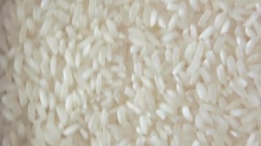 Kuru, pişmemiş, beyaz pirinç arka planı yavaşça yukarı doğru hareket ediyor. Çiğ Uzun Taneli Pirinç. Asya mutfağı ve kültürü. Sağlıklı beslenme malzemeleri. Diyet Yemekler