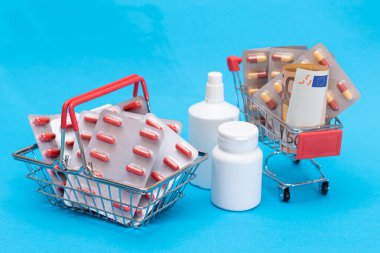 İlaç almak için. Uyuşturucu Bağımlılığı Konsepti: Mavi Arkaplan 'daki alışveriş arabasında haplar ve kapsüller. Global İlaç Endüstrisi ve Büyük İlaç. İlaç Ürünleri Siparişi