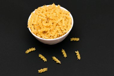 White Bowl 'daki pişmemiş Fusilli Makarna Siyah Masa' da. Çiğ ve kuru makarna. Sağlıksız ve şişman yiyecekler. İtalyan Kültürü