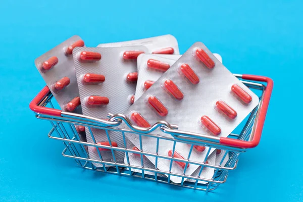Buying Medicines. Drug Addiction Concept: Pills and Capsules in Shopping Basket on Blue Background. Global Pharmaceutical Industry and Big Pharma. Ordering Pharmaceutical Products