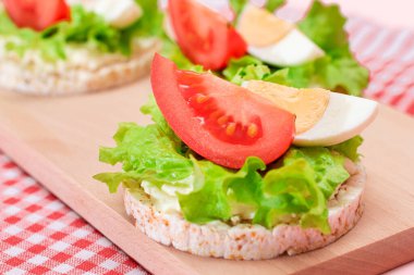 Domatesli Rice Cake Sandviç, Tahta Kesme Kurulunda Marul ve Yumurta. Kolay Kahvaltı 'da. Diyet yemek. Hızlı ve sağlıklı sandviçler. Lezzetli dolgulu kızarmış ekmek. Sağlıklı Beslenme Atıştırması
