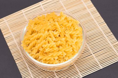 Cam kavanozda pişmemiş Fusilli Makarna Bambu Mat üzerinde Kara Arkaplanda. Şişman ve Sağlıksız Yemek. Klasik kuru sarmal makarna. İtalyan Kültür ve Mutfağı. Çiğ Makarna