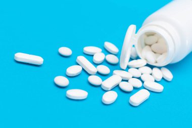 Küresel İlaç Endüstrisi ve İlaç Ürünleri - İlaç Konteynırından Dağılmış Beyaz Haplar veya Tabletler, Mavi Arkaplanda Yatanlar