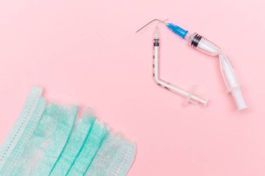 Aşı Karşıtı Hareket ve Maske Karşıtı Konsept - Kırık Tıbbi Şırınga ve Pembe Arkaplanda Yeşil Yırtık Tıbbi Maske. Salgın ve Kilitlenme Sonu - Üst Görünüm, Düz Yat